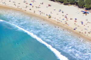 Aerial Photo Of Noosa Heads. Capturing The Turquoise Water, Sand, Swimmers And Lots Of Colourful Beach Umbrellas.